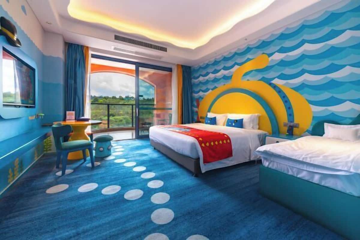 Habitación de hotel con una cama grande, una cama más pequeña, un escritorio y vistas a través de un ventanal.