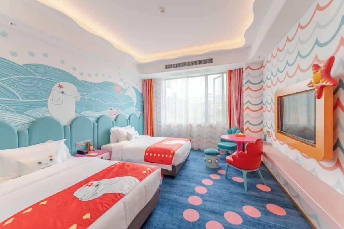 Habitación de hotel con dos camas, televisión, una mesita y un mural de pared colorido.