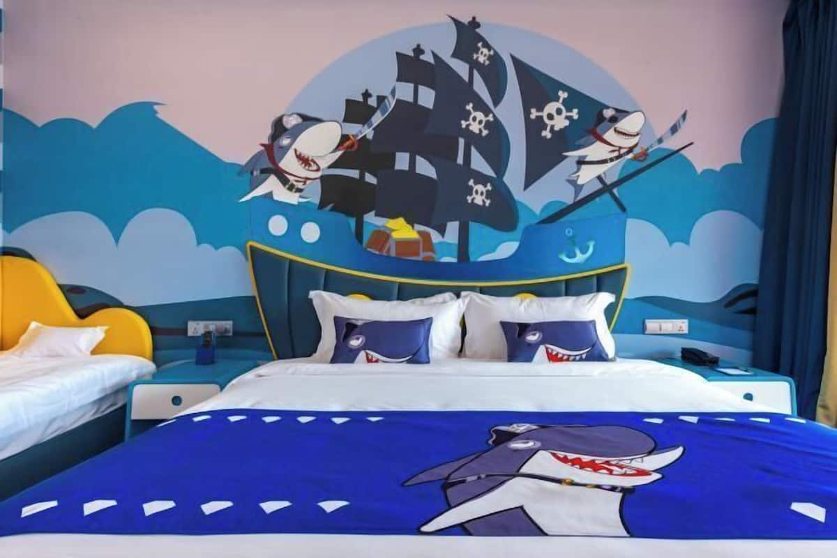 Habitación de hotel con una cama que presenta un mural con temática náutica, un sofá independiente y una mesita de noche con lámpara.