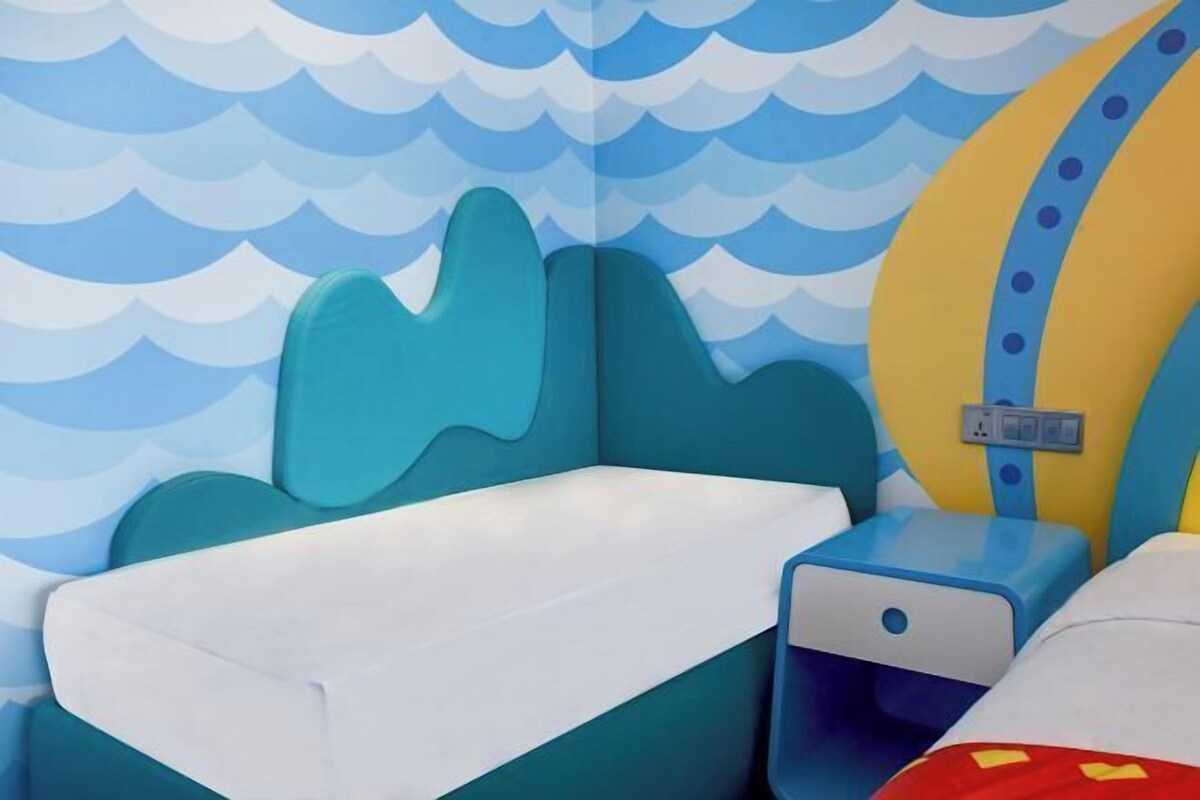 Un dormitorio infantil con un papel tapiz de diseño de olas, una cama, una mesita de noche y un enchufe.