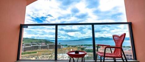 A balcony with a view of a coastal cityscape, a red chair, and a small table.