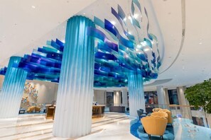 A modern lobby with a unique ceiling design, a reception desk, and comfortable seating.