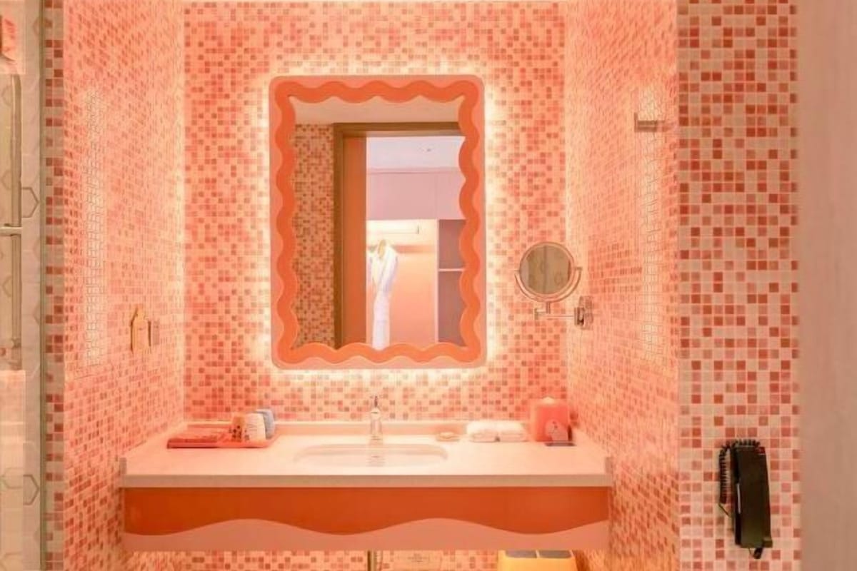 Un baño con pared de mosaico rosa, un lavamanos con espejo y un perchero para toallas.