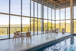 Uma área interna de piscina moderna, com grandes janelas, piscina e assentos.