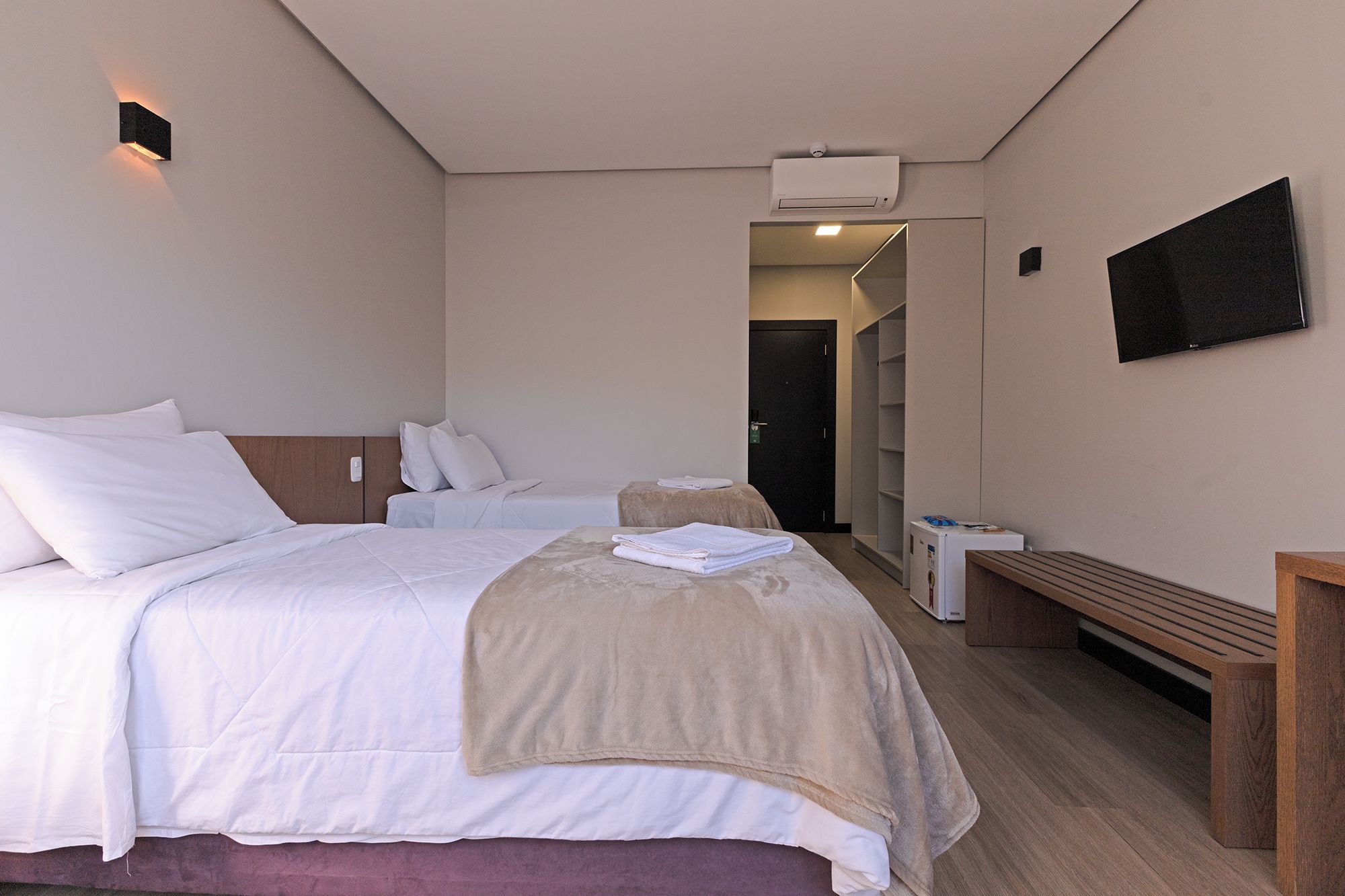 Een hotelkamer met een bed, een bankje, een televisie en een deur naar een andere kamer.