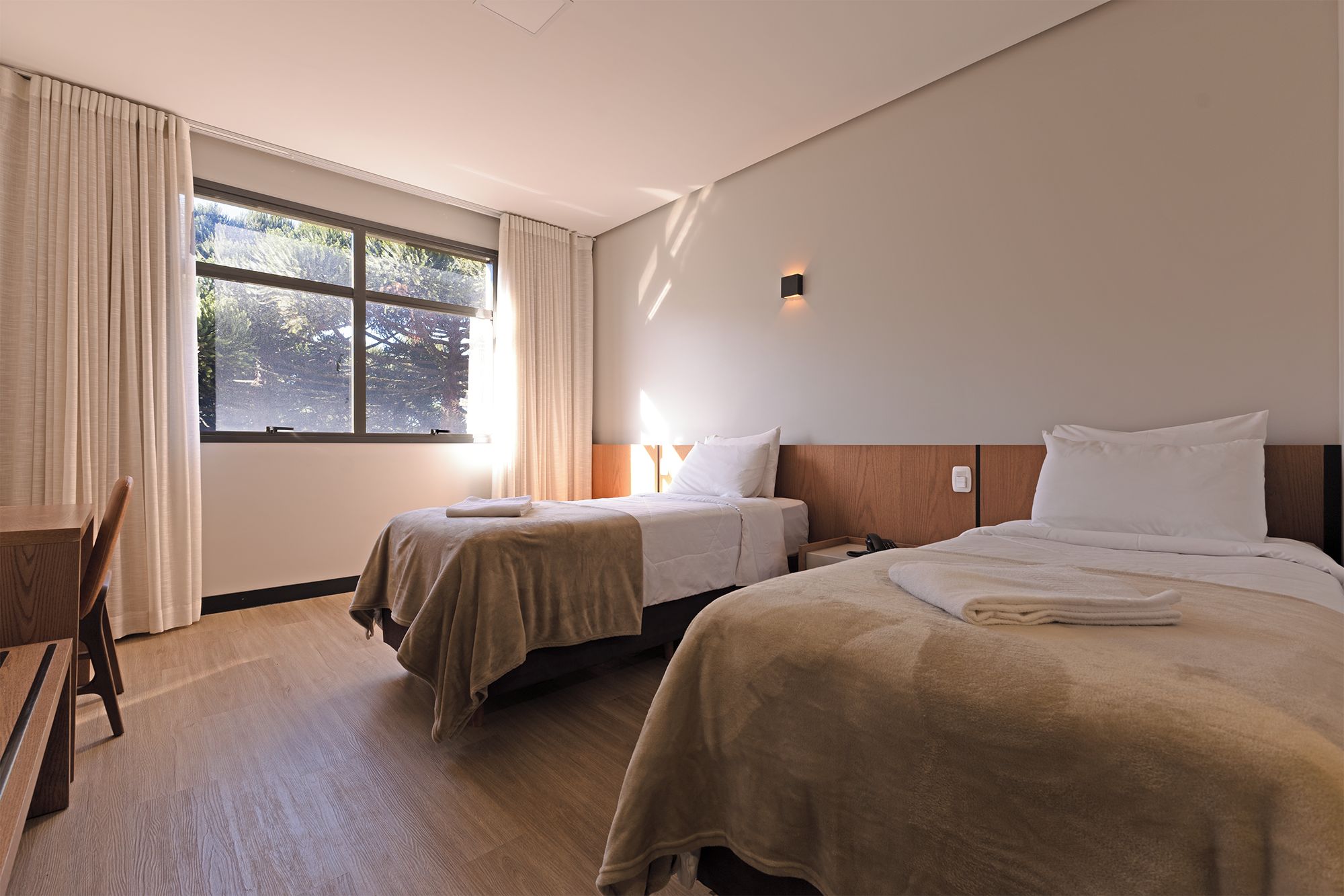 A hotel room with two beds, a wooden chair, a desk, and a window with curtains.