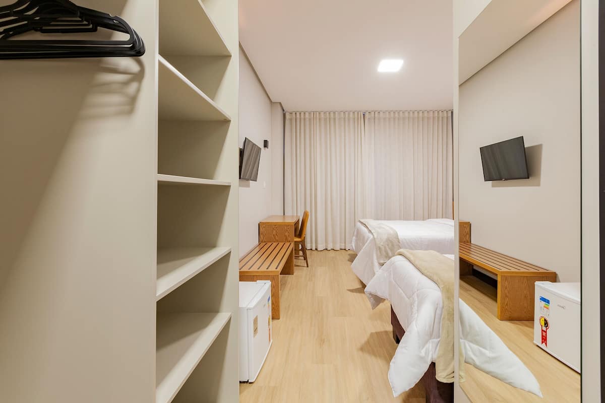 Habitación de hotel con dos camas, un escritorio, una silla, un armario y un televisor.
