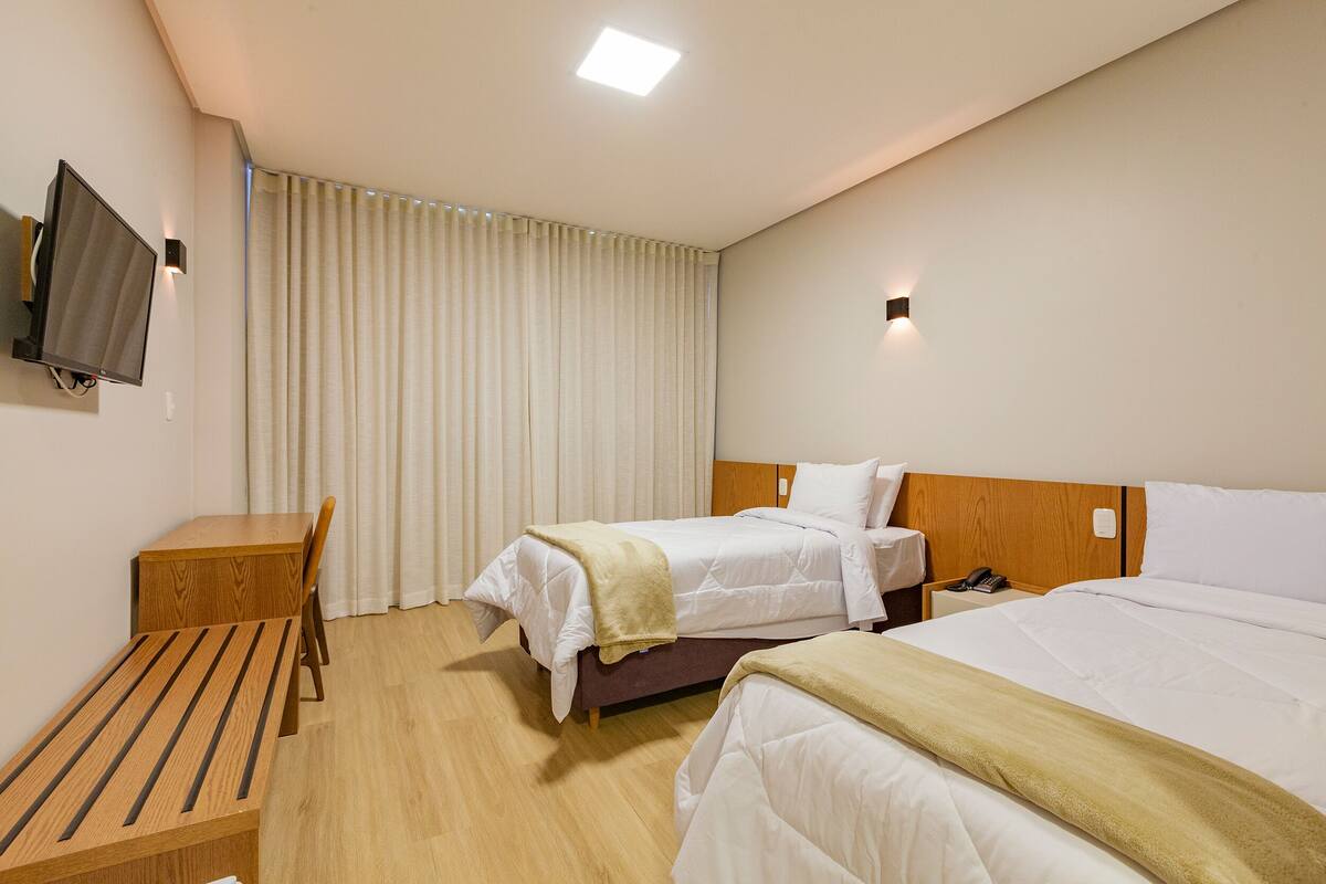 Habitación de hotel con dos camas, un escritorio, una silla, un televisor y una ventana con cortinas.