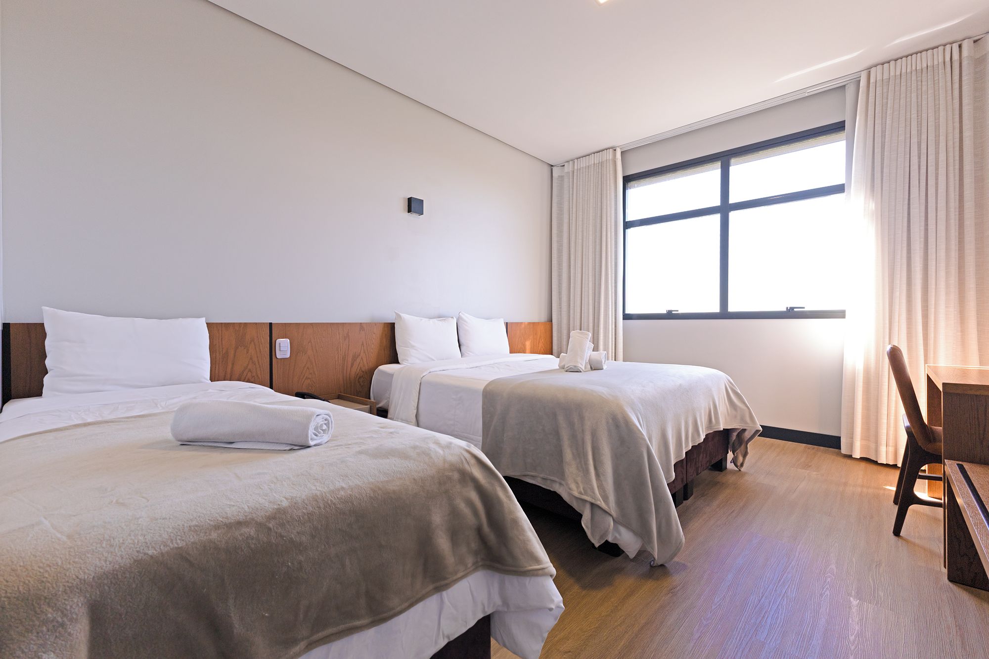 Ein Hotelzimmer mit zwei Betten, einem Schreibtisch und einem großen Fenster.