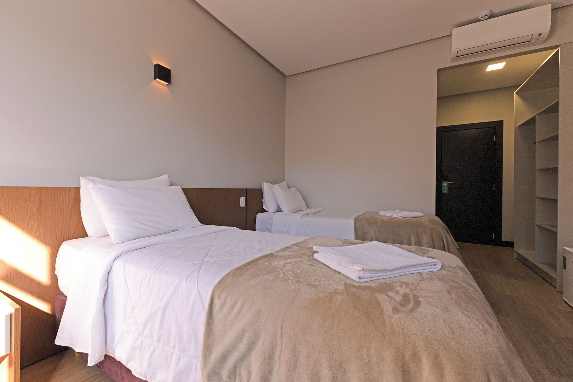 A hotel room with two beds, a wardrobe, and a bathroom.