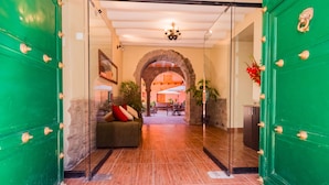 A hotel lobby with a green door, a stone archway, a sofa with cushions, and a dining area in the background. - ANAHUARQUE (Cusco)