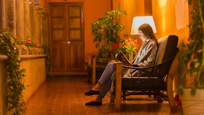 A woman sitting on a bench in a corridor with a lamp and potted plants. - ANAHUARQUE (Cusco)