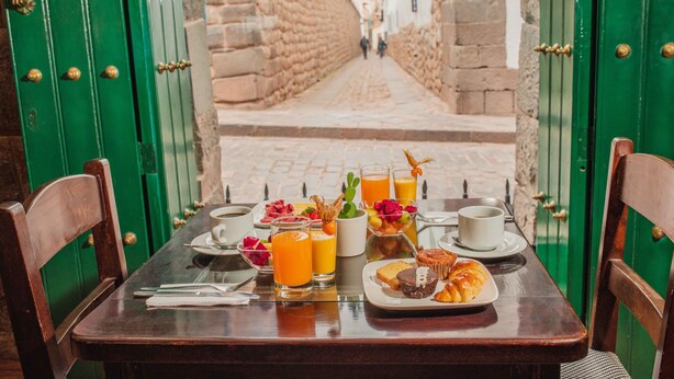 A breakfast table with plates of food, glasses of orange juice, and a cup of coffee. - ANAHUARQUE (Cusco)