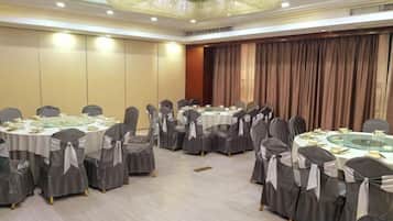 A conference room with round tables and chairs, a chandelier, and a curtain backdrop.