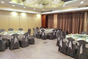 A conference room with round tables and chairs, a chandelier, and a curtain backdrop. - XM Butler Hotel (Jinjiang)