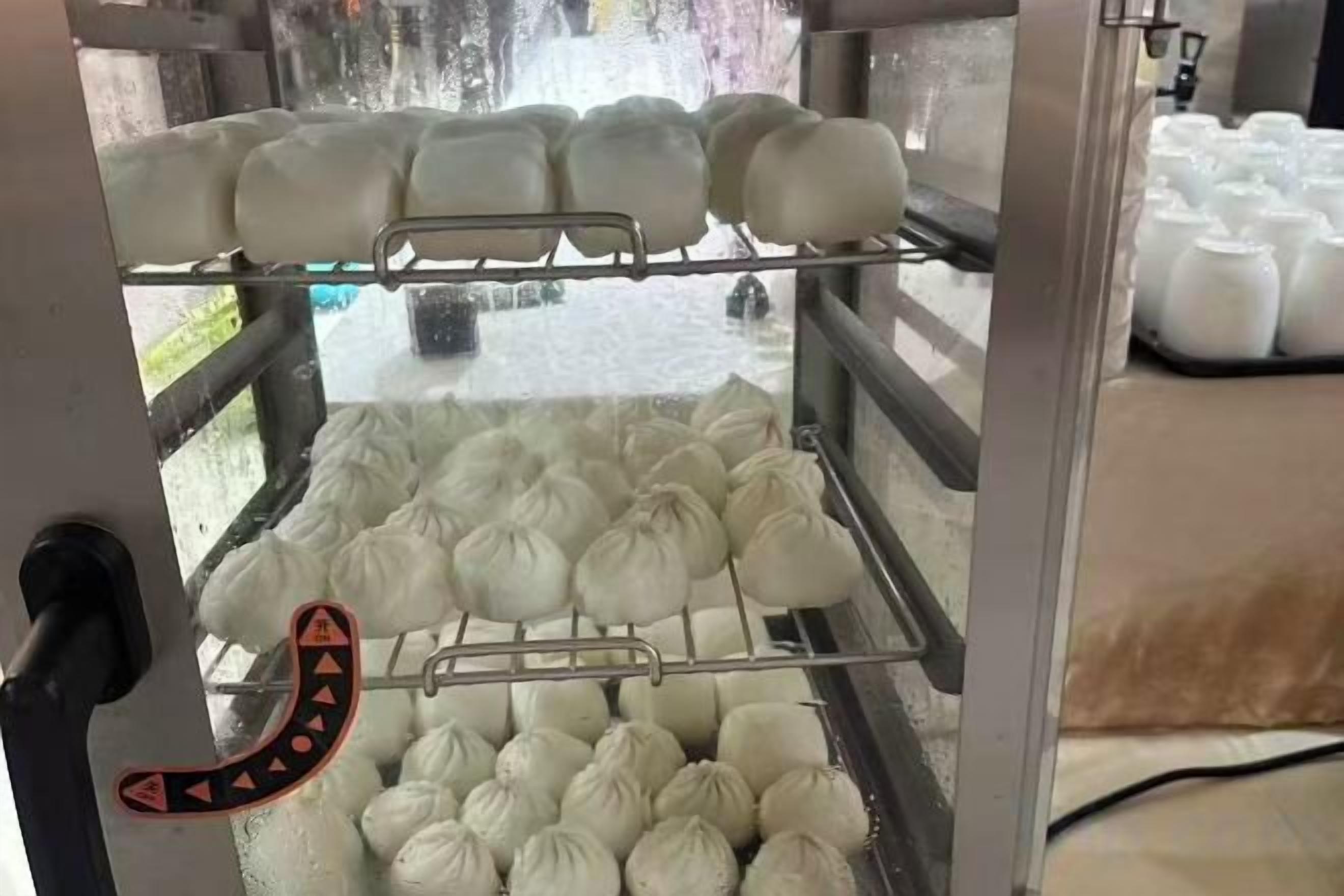 A food preparation area with a machine for making steamed buns, a metal rack, and a caution sign.