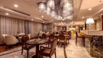Zona de dinning d'un hotel amb taules rodones, cadires i una barra.