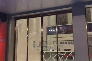 Entrada de hotel con puerta de cristal, un mostrador de recepción y un letrero con caracteres chinos.