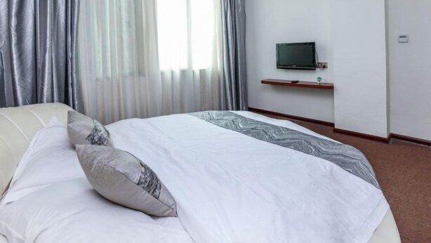 Una habitación de hotel con cama, televisión sobre un mueble y ventana con cortinas.