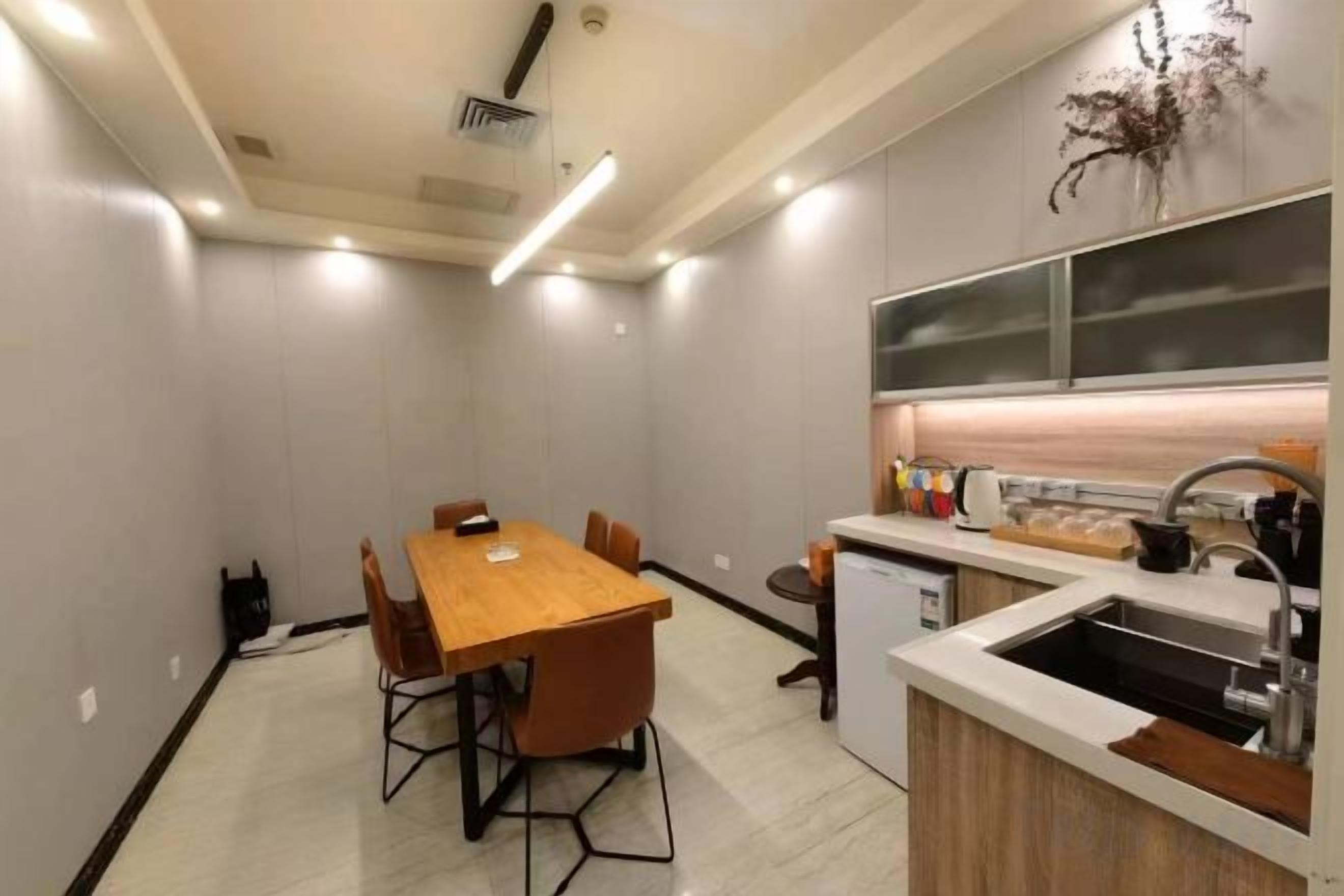 A modern kitchen with a wooden dining table and chairs, a built-in oven, and a small refrigerator.