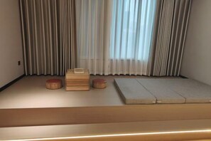 A room with tatami flooring, a low platform, and a window with sheer curtains.