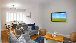 A modern living room with a grey sofa, a wooden coffee table, and a TV on the wall. - Sandholme Cottage - Central location, great for families (Filey)