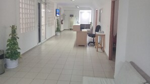 En gang med receptionsdisk, en computer og en stol. Der står plantekasser og der er et fjernsyn.