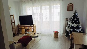 Ein Wohnzimmer mit Fernseher, Holzmöbeln, einem Weihnachtsbaum und einem Fenster mit transparenten Vorhängen.