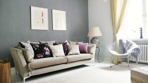 Una sala de estar con un sofá color beige, un plaid estampado, una lámpara y un sillón con una manta.