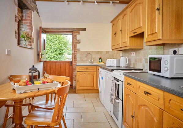 A kitchen with wooden cabinets, a washing machine, a microwave, and a dining table with chairs.