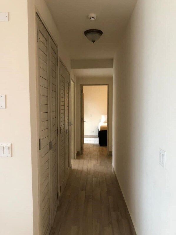 Un couloir étroit doté d’un plancher en bois, de murs blancs et d’un luminaire au plafond.