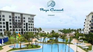 A resort pool area with a large central pool, surrounded by palm trees and lounge chairs. - Playa Caracol Residences 1 and Beach Club Chame Banks (La Boca de Chame)