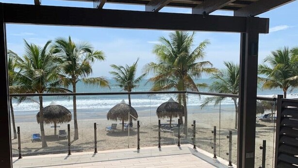 A beachside patio with a lounge chair, palm trees, and a view of the ocean. - Playa Caracol Residences 1 and Beach Club Chame Banks (La Boca de Chame)