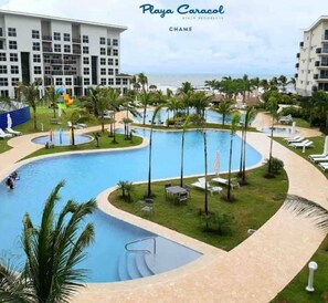 Ein Poolbereich eines Resorts mit einem großen zentralen Pool, umgeben von Palmen und Liegestühlen.