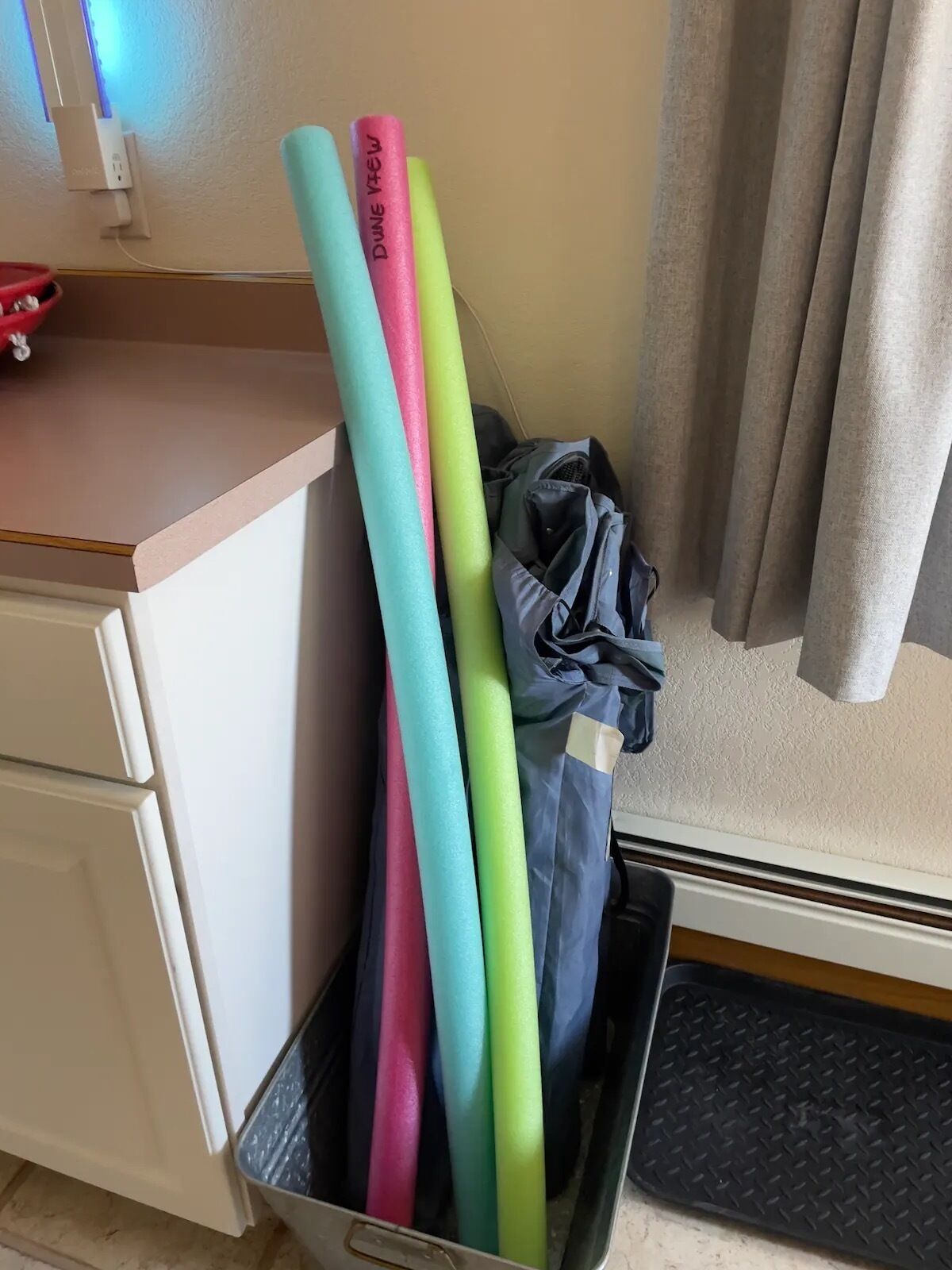 A storage bin containing colorful foam rollers labeled 'DUNE VIEW' and a black bag.