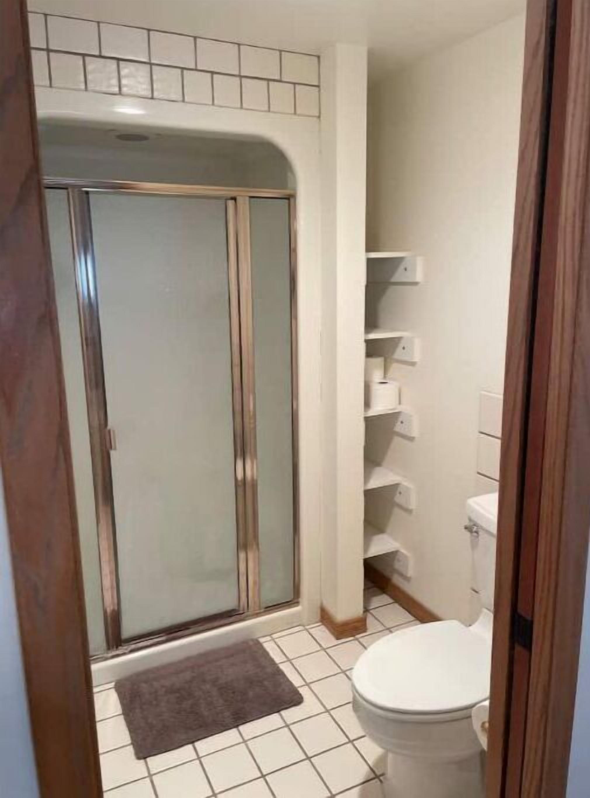 A bathroom with a shower, toilet, and shelves.