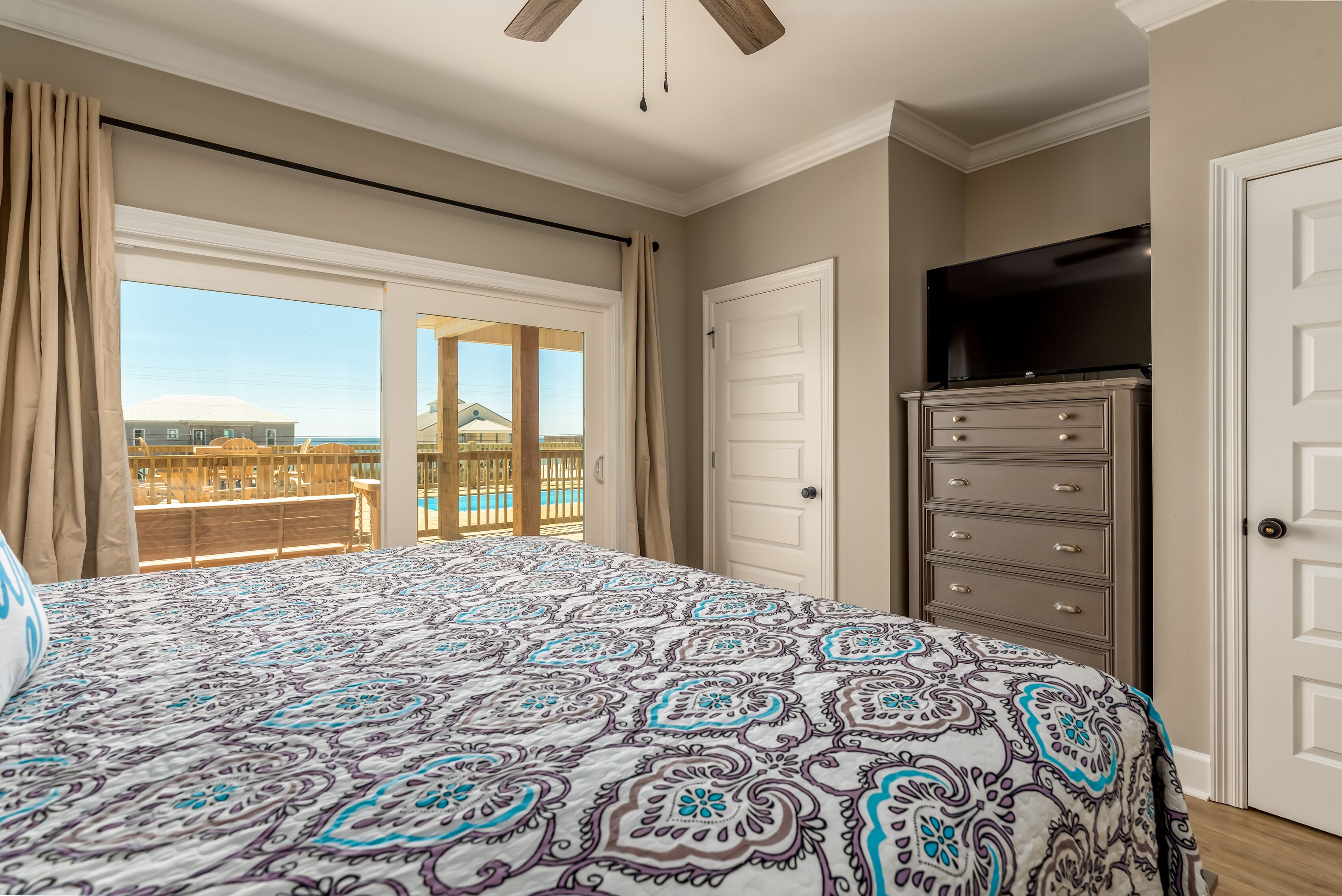 A bedroom with a large bed, a dresser, a TV, and a sliding glass door to a balcony.