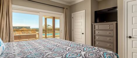 A bedroom with a large bed, a dresser, a TV, and a sliding glass door to a balcony.