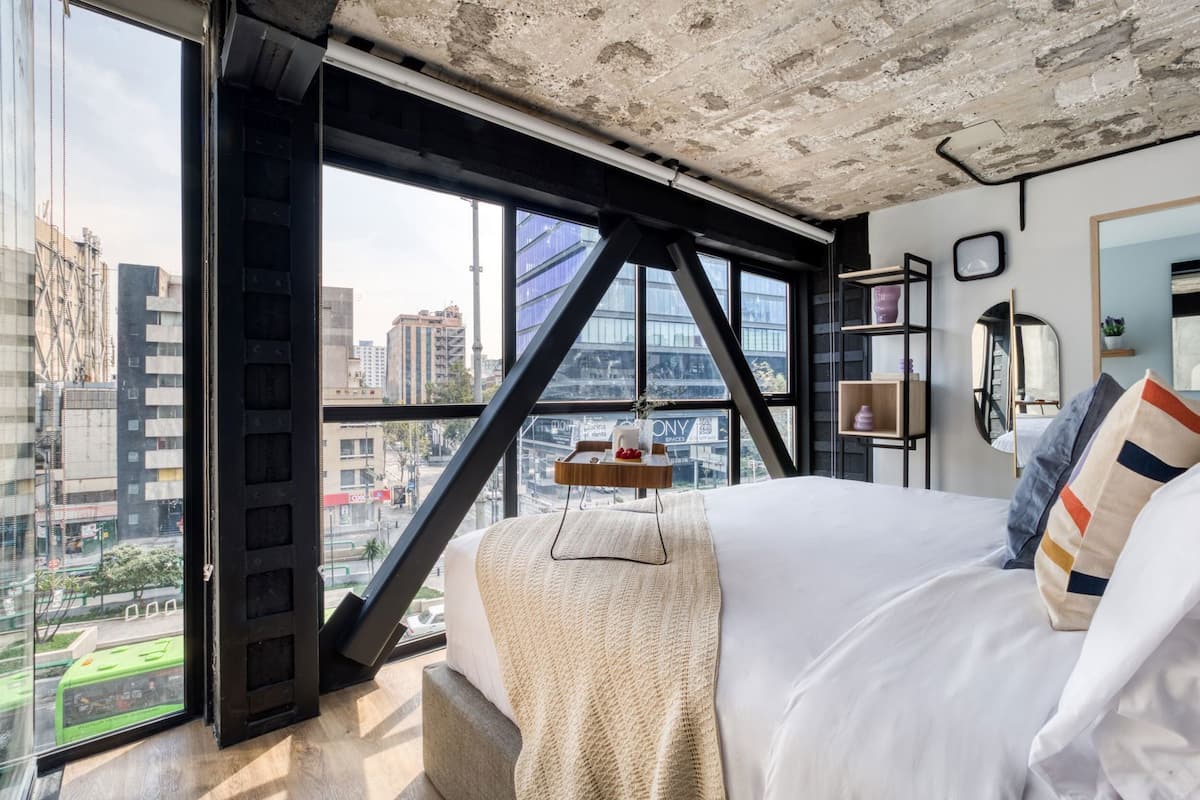 A modern bedroom with a large window, a bed, and a view of the cityscape.