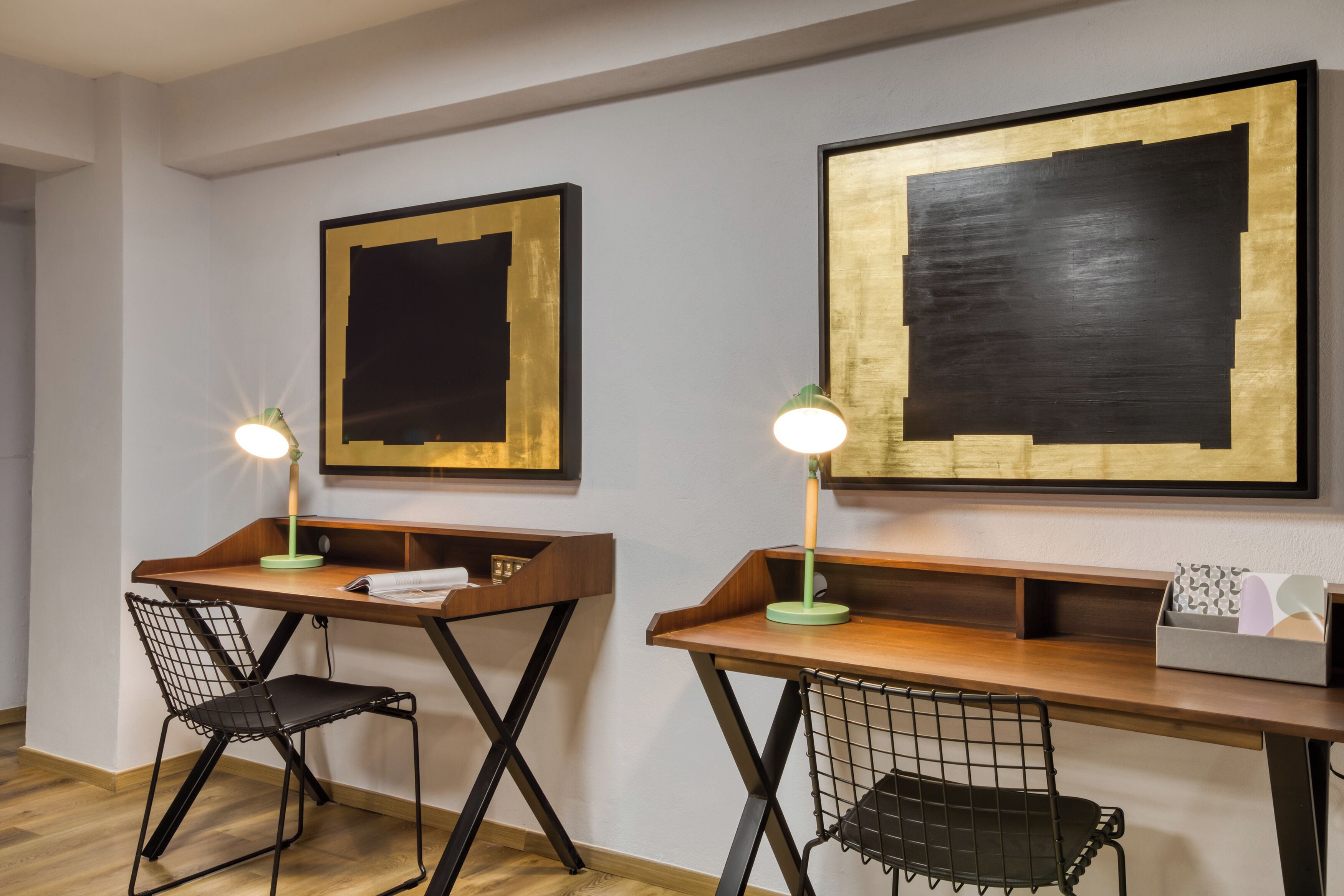 A modern room with two desks, each with a chair, and framed artworks on the wall.