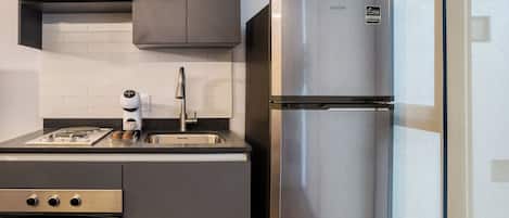 A compact kitchen with a stainless steel refrigerator, a built-in oven, and a modern faucet.