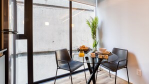 A modern dining area with a glass table, two black chairs, a plant, and breakfast items. - ULIV El Ángel (Mexico City)