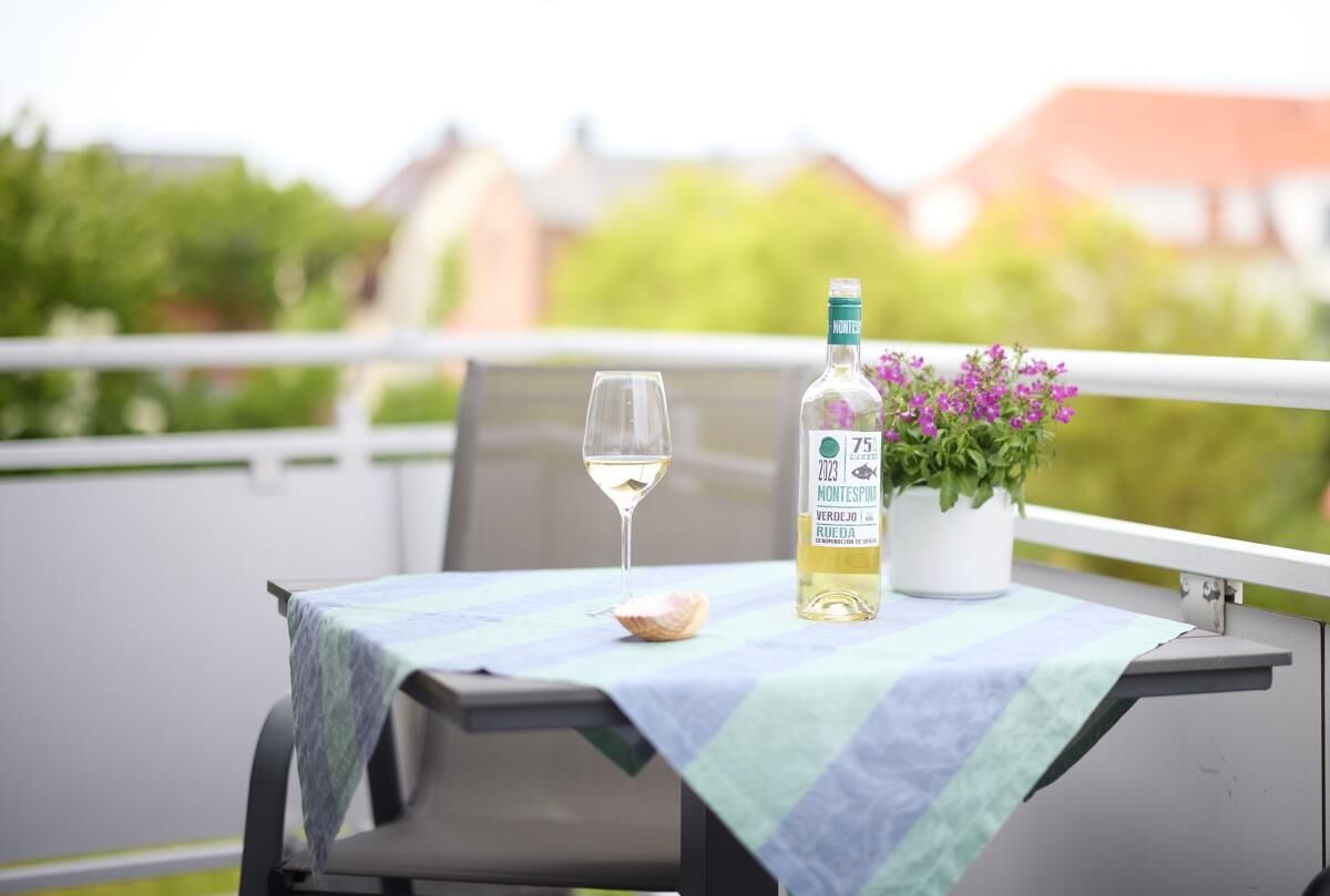 A table with a bottle of Montespin 2023 wine, a glass, and a potted plant on a balcony.