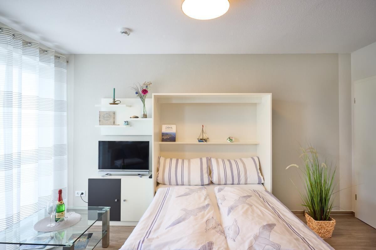 Quarto moderno com cama, televisão, escrivaninha e planta.
