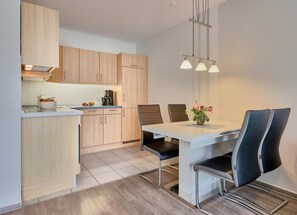 Une cuisine moderne avec des meubles en bois, une table à manger avec des chaises et des luminaires suspendus.