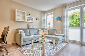 Un salon comprenant un canapé, une table basse en verre, un tapis à motifs, un meuble avec des portes en verre et une fenêtre avec des rideaux.