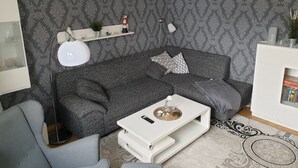 A modern living room with a grey patterned wallpaper, a grey sofa, a white coffee table, and a floor lamp.