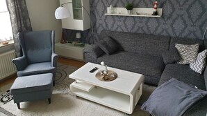 A living room with a grey sofa, a blue armchair, a white coffee table, and a white cabinet against a patterned wallpaper.