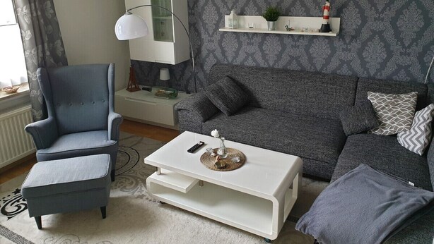 A living room with a grey sofa, a blue armchair, a white coffee table, and a white cabinet against a patterned wallpaper.