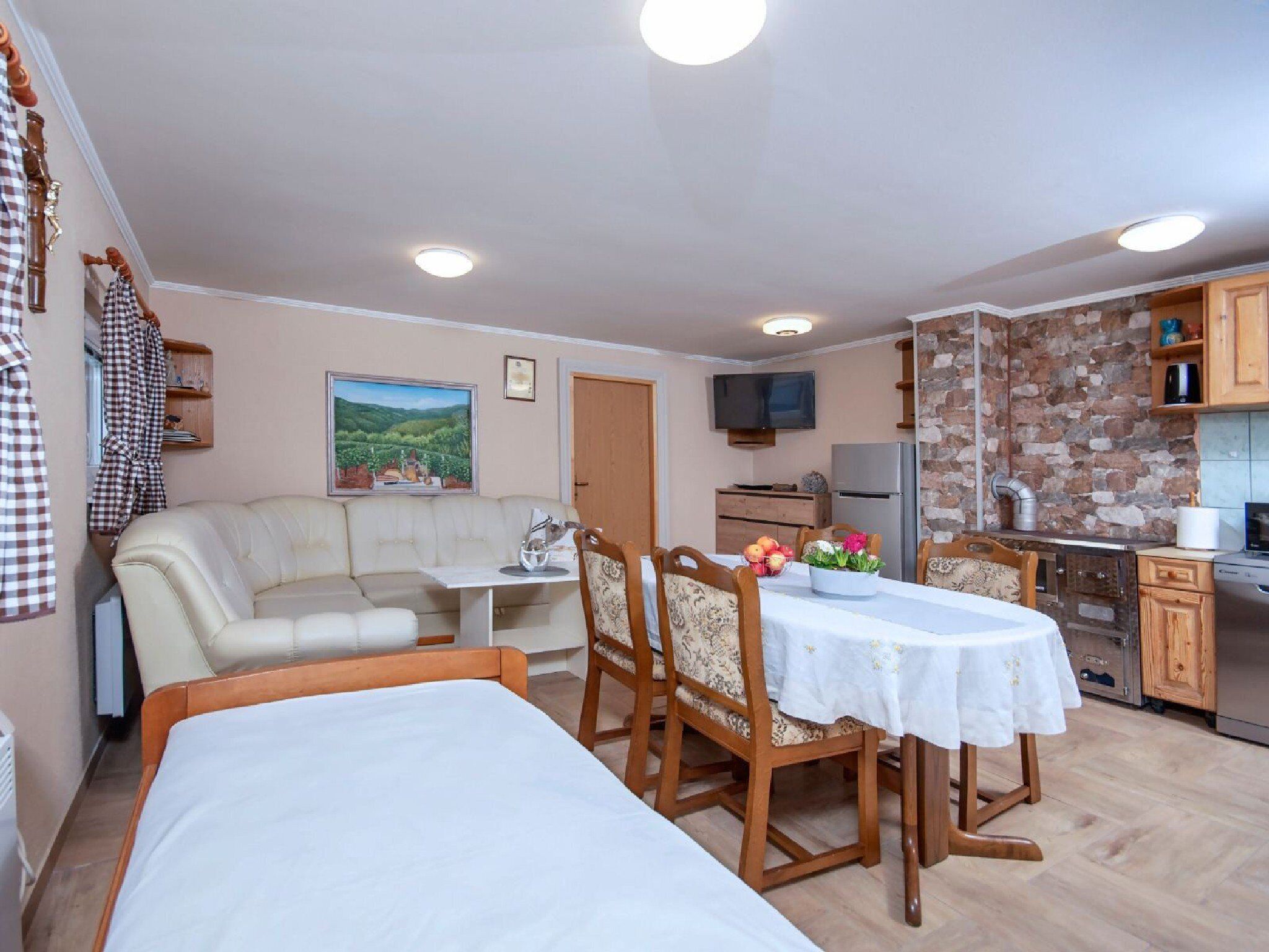 Une pièce confortable comprenant un lit, un canapé, une table à manger avec des chaises, un coin cuisine avec un réfrigérateur et une cuisinière, et un téléviseur fixé au mur.
